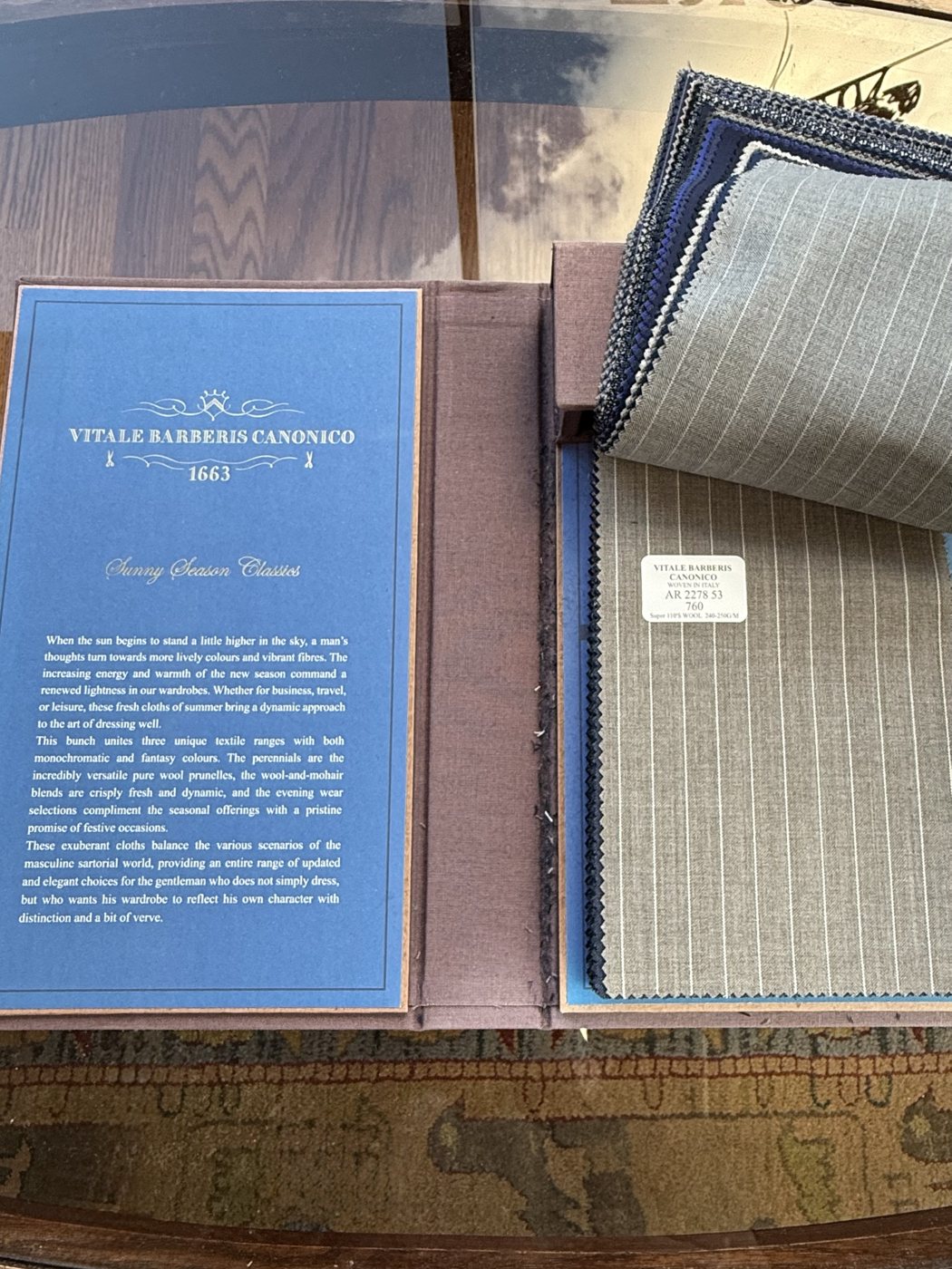 A Vitale Barberis Canonico cloth sample book open on a table, with pinstriped grey wool swatches fanned out beside the brand card